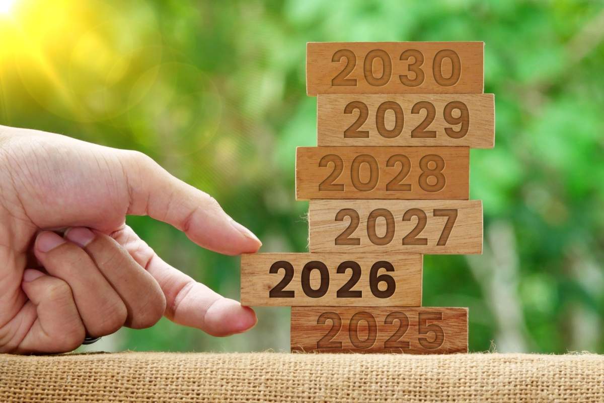 Mână trăgând un bloc de lemn pe care scrie 2026 pe un turn de lemn cu numerele 2025-2030. Strategie de afaceri. Concept de Anul Nou