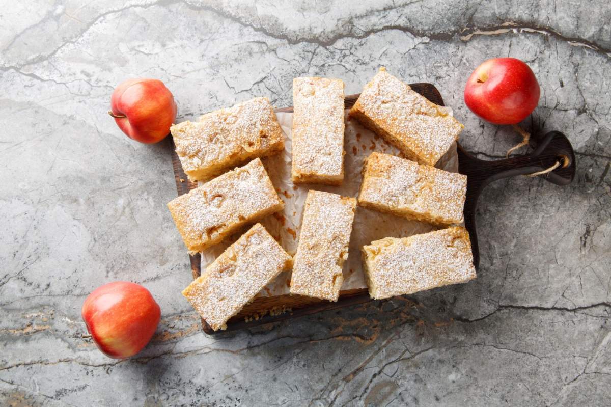 Prăjitură cu sos de mere și condimente calde, precum cuișoare, ghimbir și scorțișoară, în prim-plan pe o tăblie de lemn așezată pe o masă. Vedere orizontală de sus.