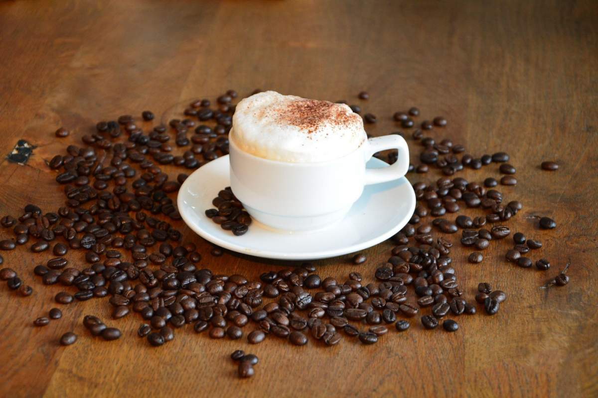 O ceașcă de cafea fierbinte cu decorare cu ingrediente, pusă pe masa maro