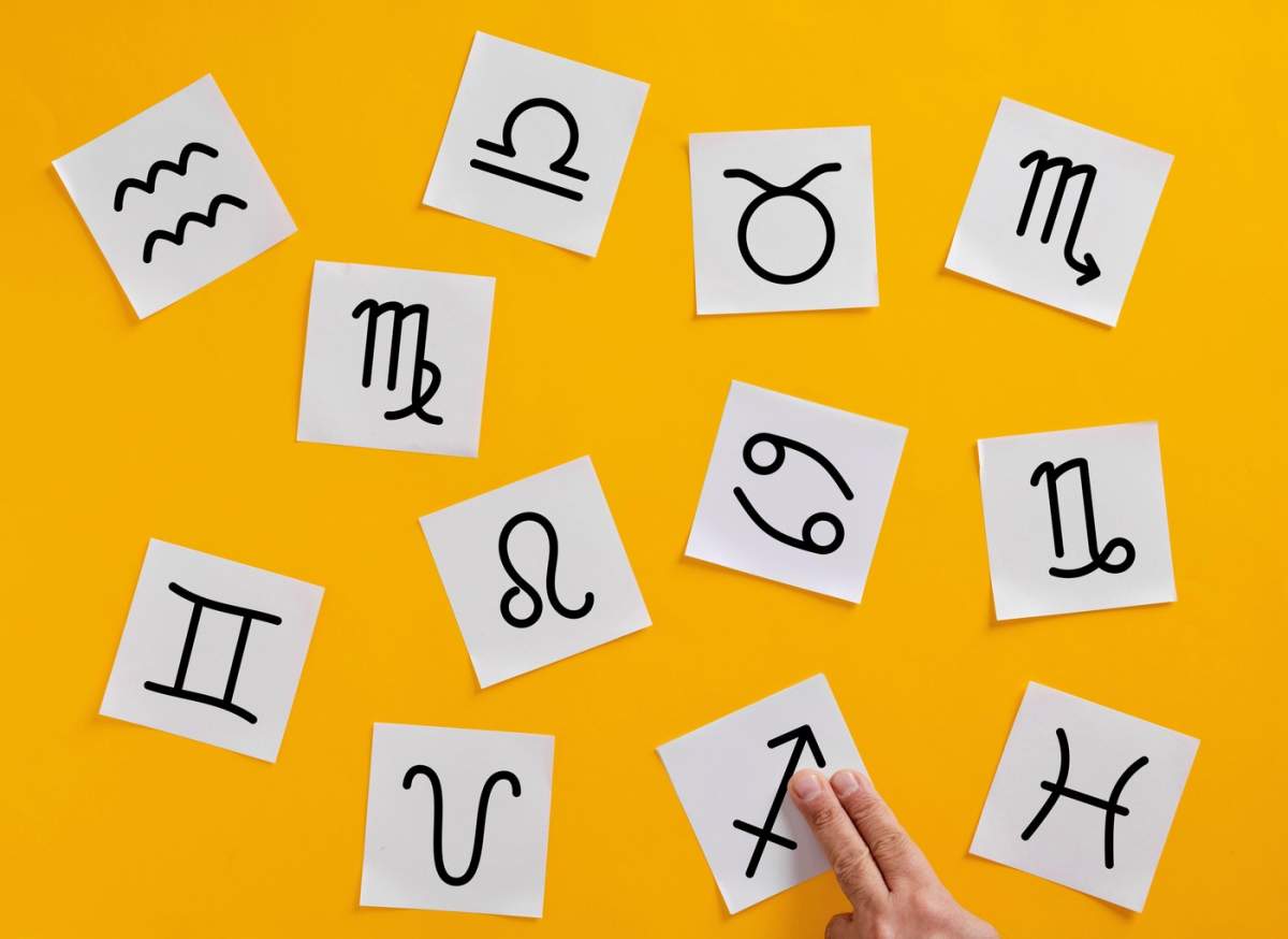 Mâna unui astrolog care aranjează cu îndemânare semnele zodiacale pe un fundal galben vibrant, capturând esența astrologiei și a misticismului