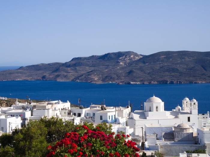 Vedere panoramică a Plaka de pe insula Milos, Cyclades, cu arhitectură albă, gerani roz, Marea Egee și golf montan