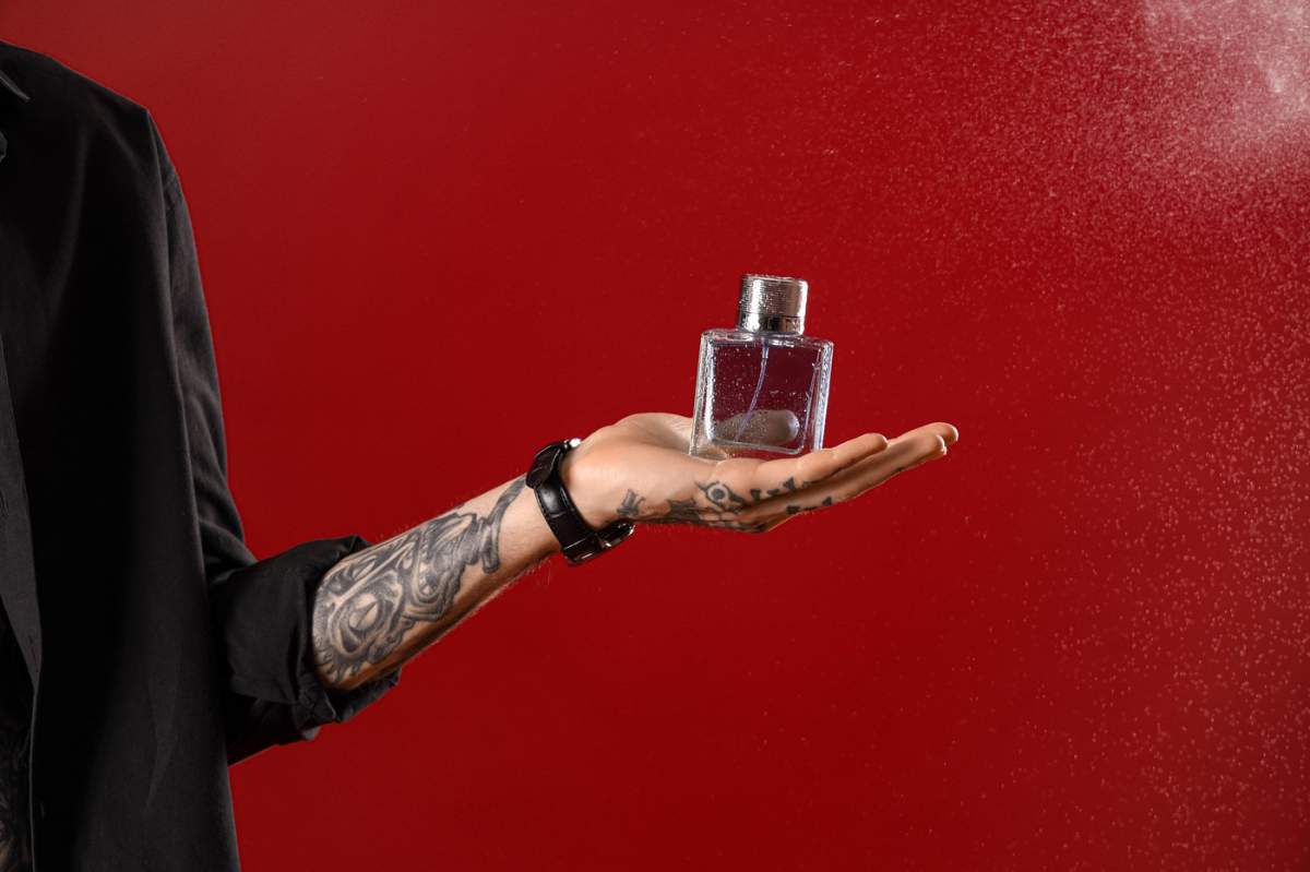 Tânăr tatuat cu parfum pe fundal roșu, prim-plan