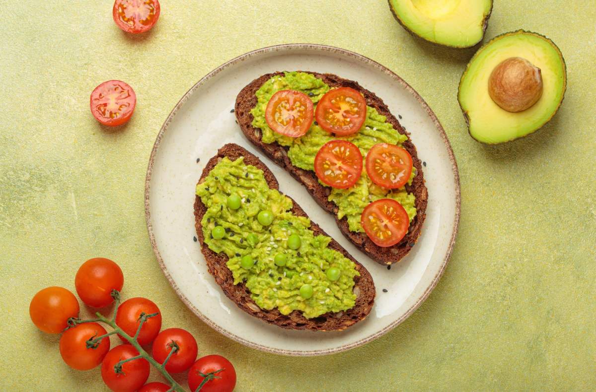 Sănătos avocado toast cu mazăre verde și roșii cherry pe întreaga pâine de secară vedere de sus pe fundal verde deschis