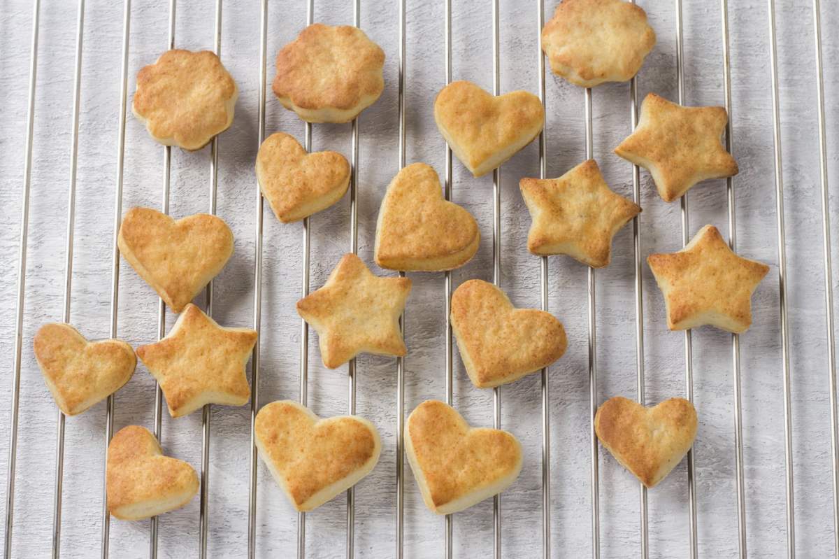 Alimente, biscuiți proaspăt coapte cu brânză de vaci în formă de stele și inimi pe o grilă de oțel, vedere de sus. Etapa de preparare a delicioșilor biscuiți de casă.