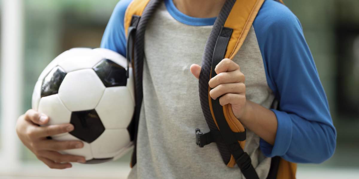 Un băiețel cu o minge de fotbal este însoțit de mama sa în timp ce merg spre școală, împărtășind zâmbete și entuziasm pentru ziua care urmează.