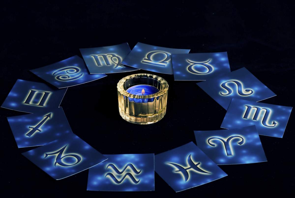 Cărți albastre cu semne zodiacale aranjate în cerc în jurul unei lumânări aprinse