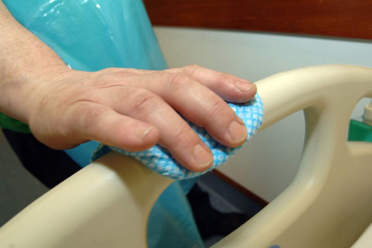 O imagine în prim-plan cu un angajat al serviciului de curățenie dintr-un spital care curăță un pat pentru a preveni răspândirea infecțiilor în unitatea spitalicească.