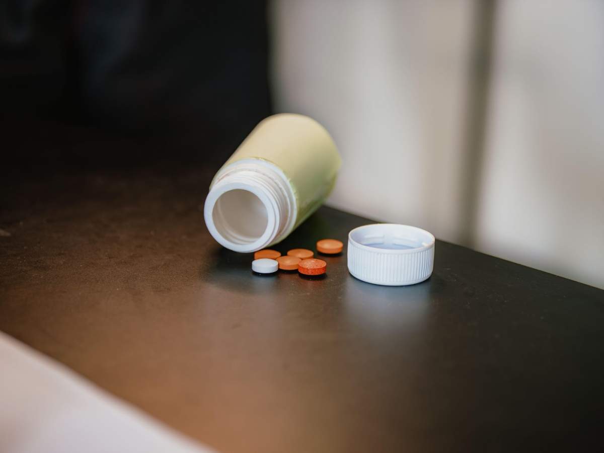 Fotografie în prim-plan a unui flacon de medicamente deschis, cu pastile vărsate pe o suprafață întunecată. Potrivit pentru ilustrarea sănătății, farmaciei, tratamentului, dozajului, medicamentelor.