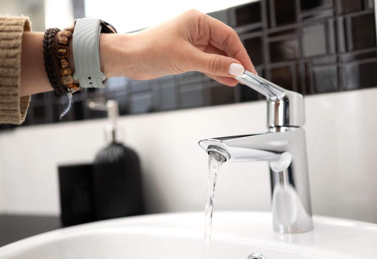 Fată deschide robinetul de la chiuveta din baie și apa curge din robinet