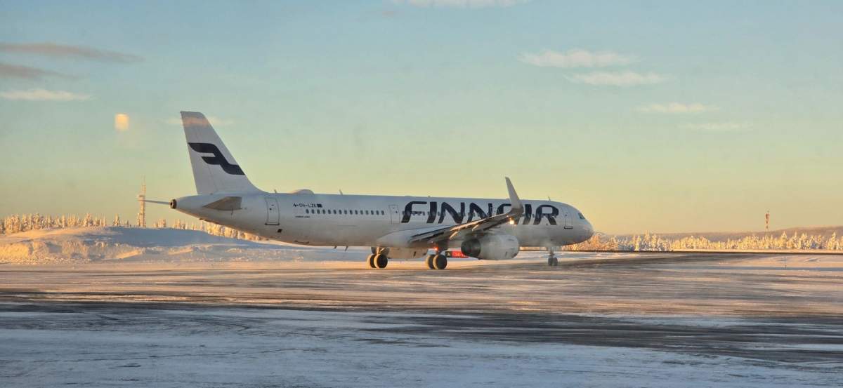 Un zbor Finnair stă pe pista aeroportului Kittil din Laponia, Finlanda. Peisajul de iarnă uimitor strălucește sub soarele dimineții devreme.