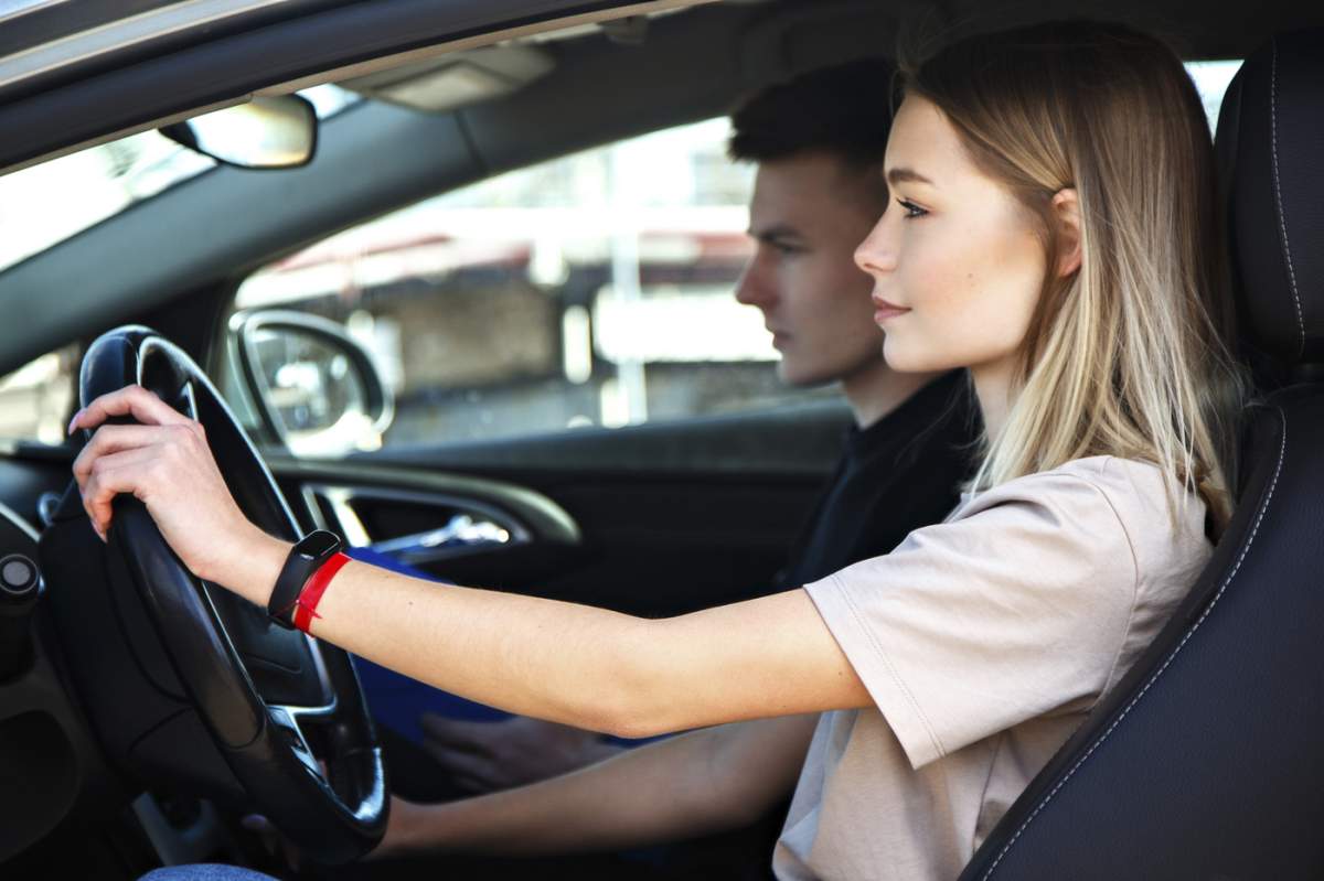 Șoferul este instructor de la o școală auto, iar elevă se află pe o mașină de examen. Lecție la circuit.