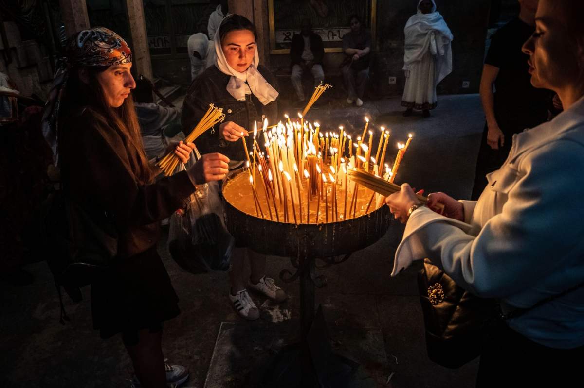 Pelerini creștini aprinzând lumânări de rugăciune în întunericul mistic și sacru al Bisericii Sfântului Mormânt. Atmosferă spirituală și profundă fervoare religioasă.