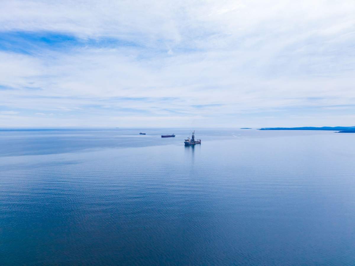 Un petrolier se deplasează pe marea deschisă sub un cer senin. Alte nave sunt vizibile în depărtare, ilustrând activitatea maritimă din timpul zilei.