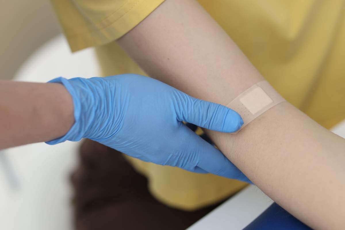 O asistentă medicală aplicând un plasture pe brațul unui pacient după recoltarea unei probe de sânge într-o clinică, prim-plan