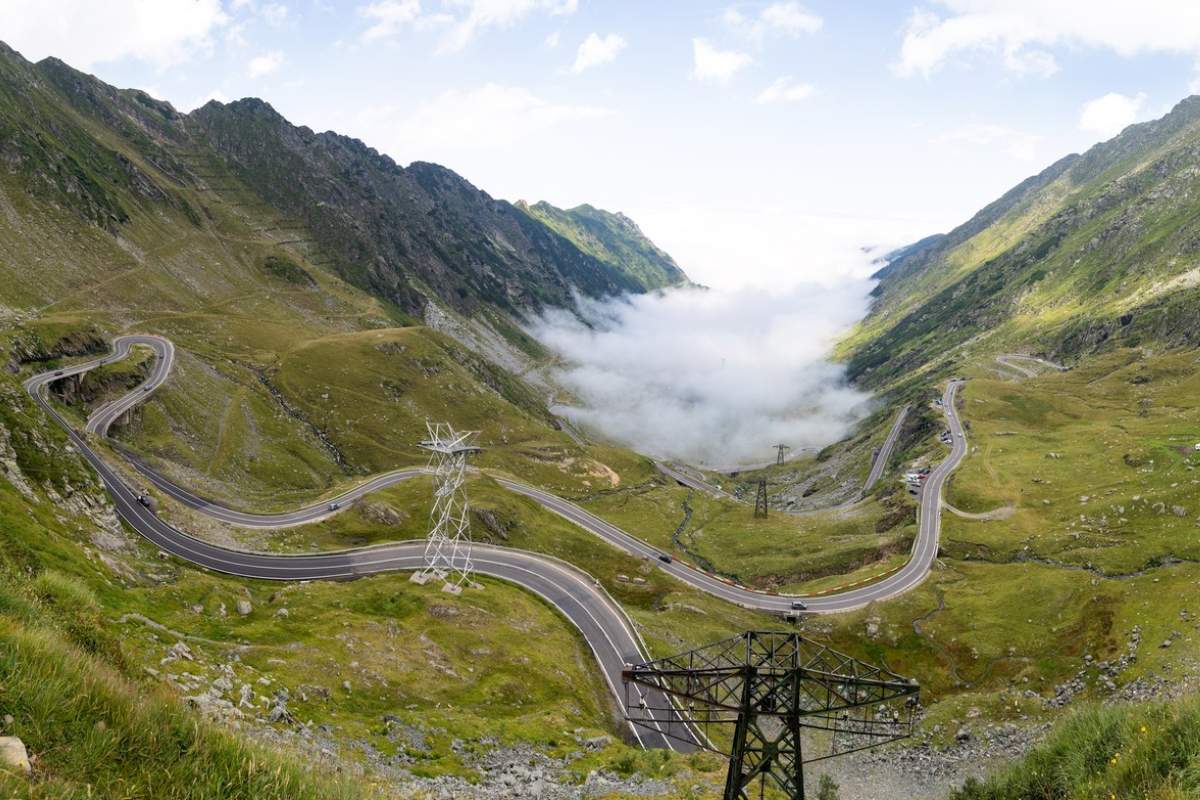 Drumul Transfăgărășan șerpuiește prin Munții Carpați, cu nori în valea de dedesubt