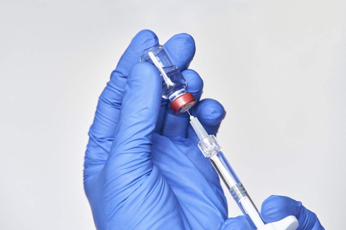 Doctor ținând o sticlă cu injecție în mâini cu mănuși albastre. Concept de gripă în laborator farmaceutic