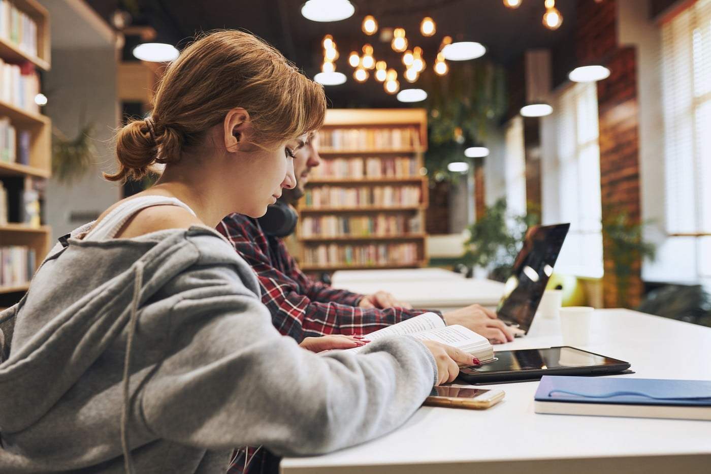 Studenți învățând în biblioteca universitară. Tânăr pregătindu-se pentru test pe laptop