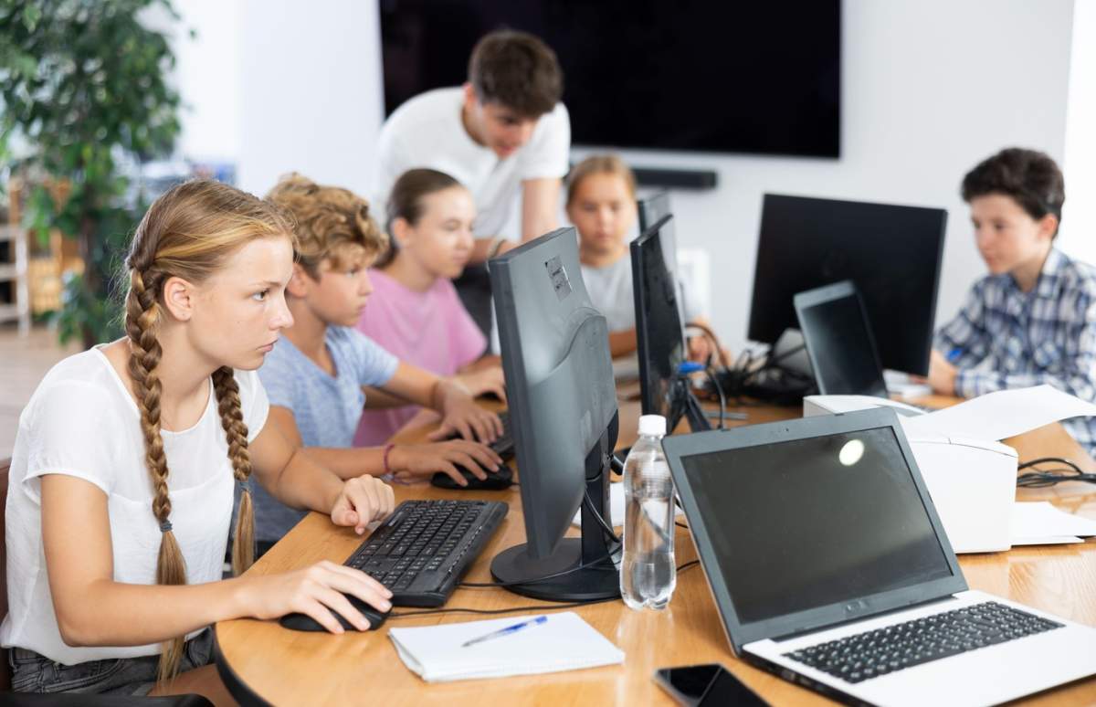 Portret de elevă adolescentă stând la masă la ora de informatică în timpul lecției, zâmbind la cameră