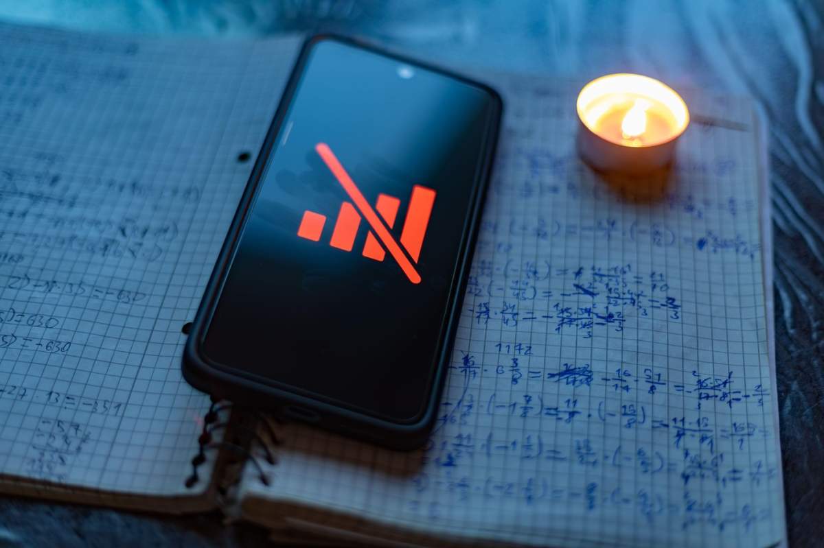 Pana de curent și lipsa semnalului în timpul războiului: un smartphone fără pictograma de rețea pe un caiet de matematică, la lumina lumânării Utilizare selectivă