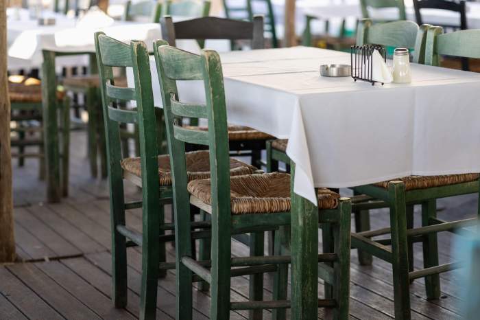 decor tradițional de tavernă grecească, cu scaune din lemn verde și scaune din paie împletite în jurul unei mese cu față albă, pe o terasă rustică din lemn, creând un...