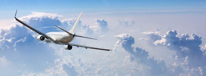 Panoramă cu un avion pe cerul albastru și printre nori